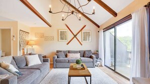 Un salón amplio con un sofá gris, una mesa de centro de madera y un ventanal con cortinas.