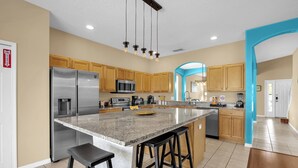 A modern kitchen with a central island, stainless steel appliances, wooden cabinets, and a blue accent wall. - Pool, Themed Rooms, Resort (Kissimmee)