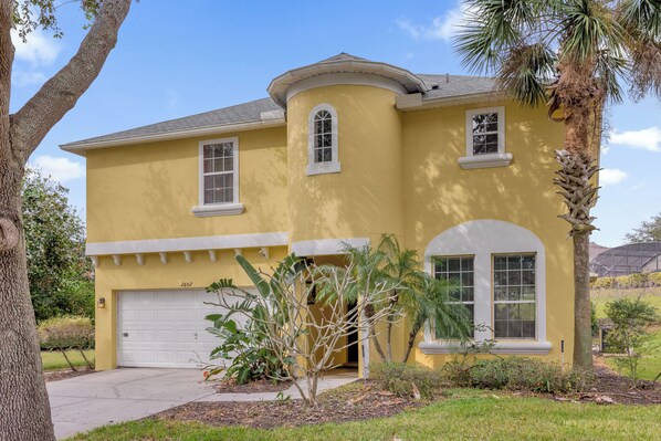 A yellow house with a garage, a small porch, and a palm tree. - Pool, Themed Rooms, Resort (Kissimmee)