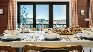 A dining table set with plates, glasses, and cutlery, with a scenic view through large windows.