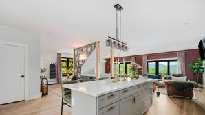 A modern kitchen with a central island, a staircase leading to an upper level, and a living area with a sofa and a TV.