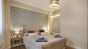 Un dormitorio con una cama grande, lámparas de noche, un espejo y un papel tapiz estampado.