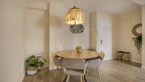 Un comedor con una mesa redonda de madera, seis sillas, una lámpara colgante y dos macetas.