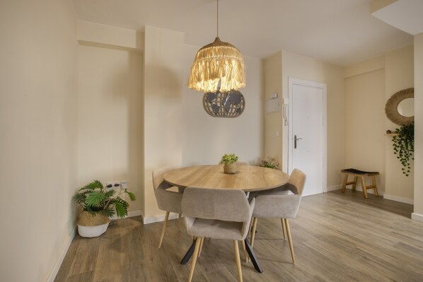 A dining area with a round wooden table, six chairs, a hanging light fixture, and two potted plants.