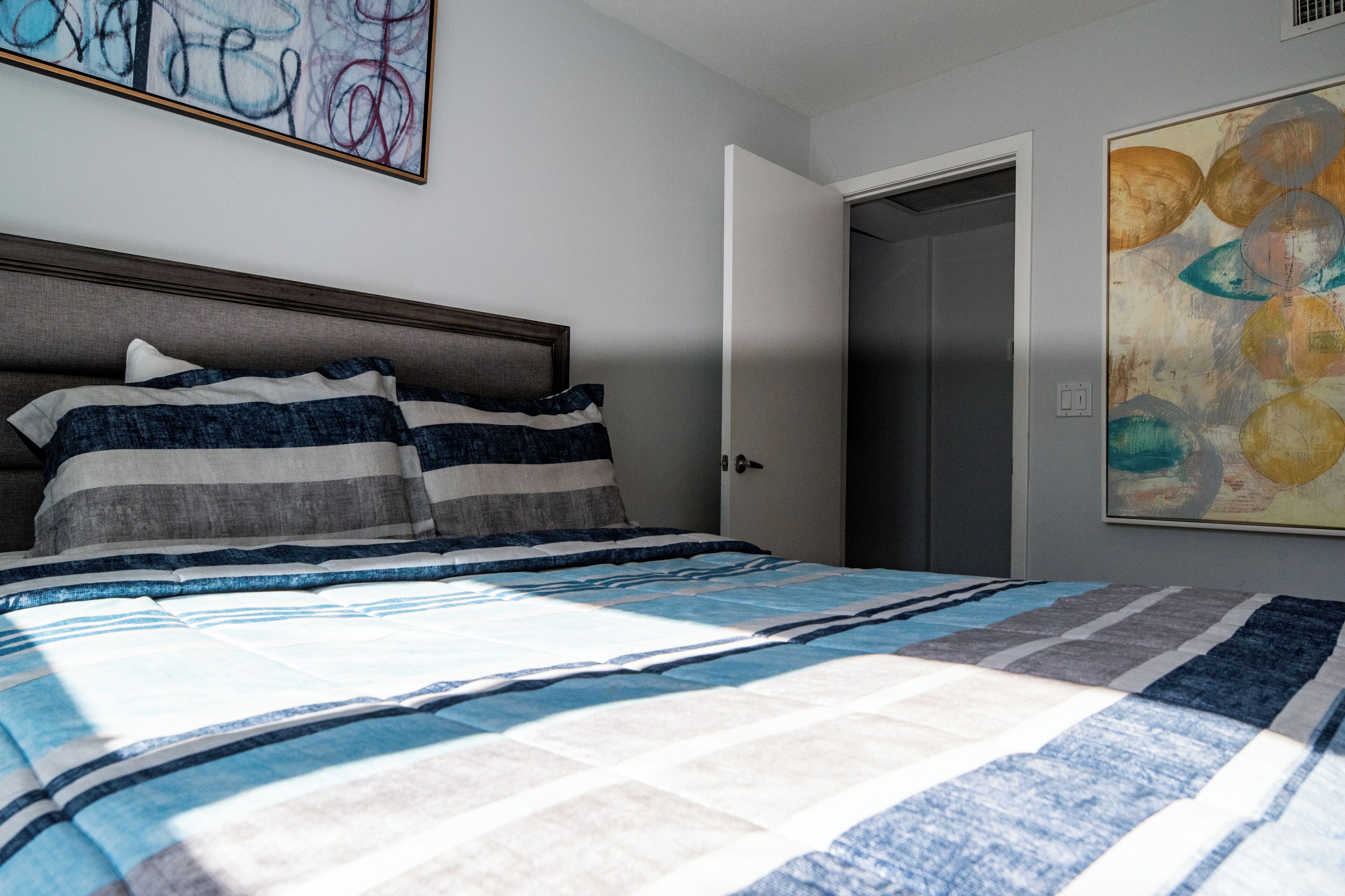 A bedroom with a bed, a door, and a wall with abstract art.