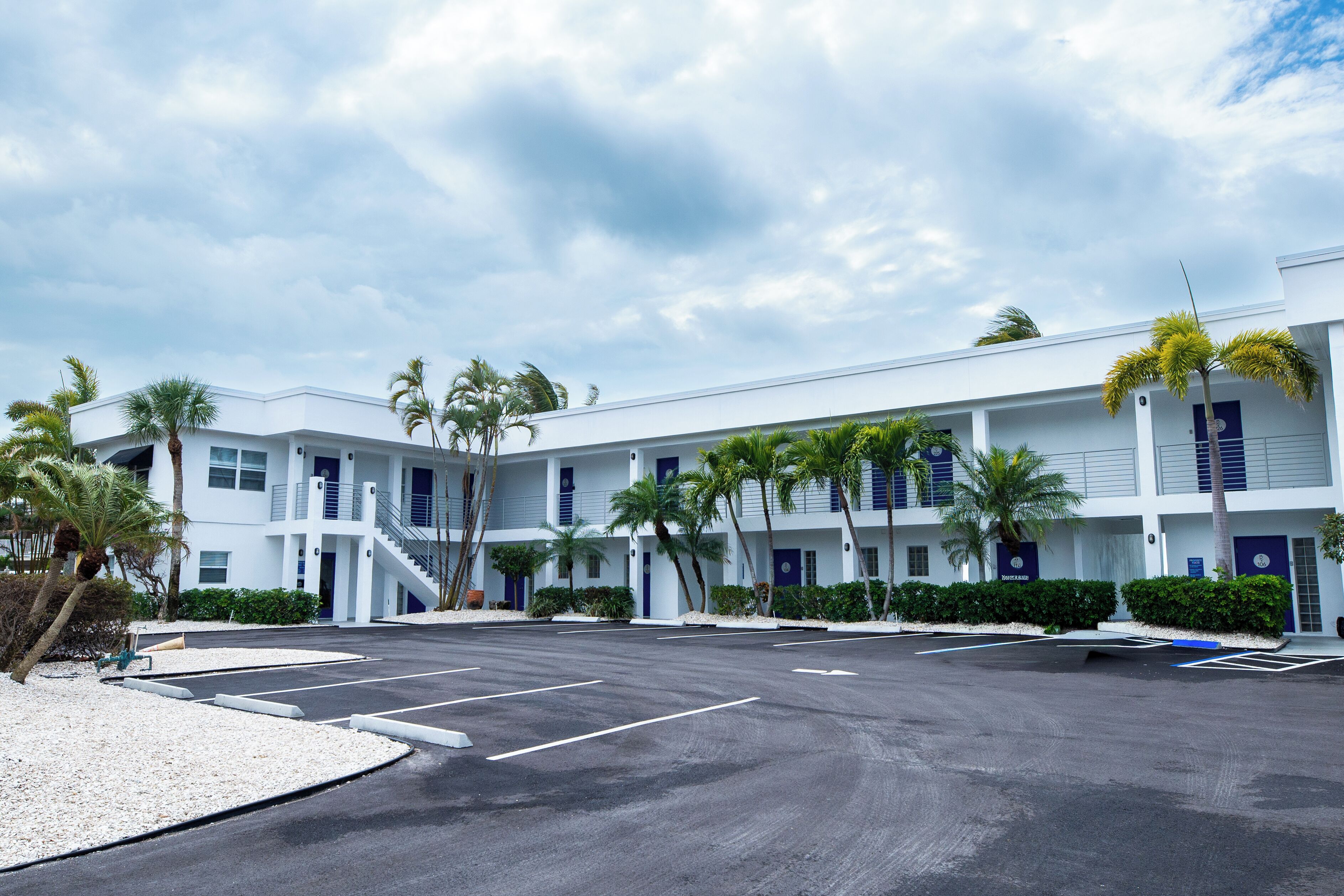 A multi-story hotel with a parking lot, palm trees, and a clear sky.
