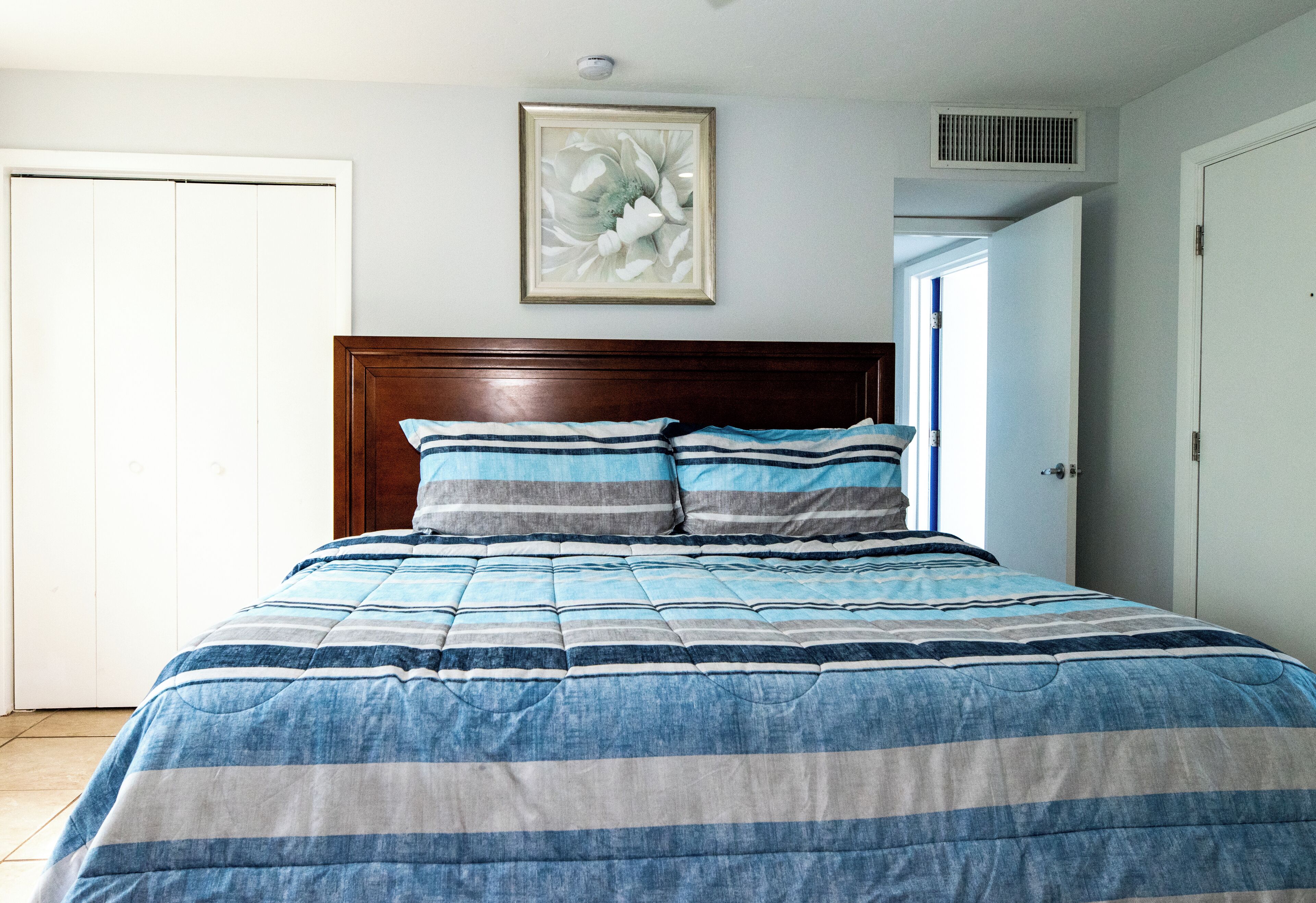 A bedroom with a bed, a headboard, a framed picture on the wall, and a door.