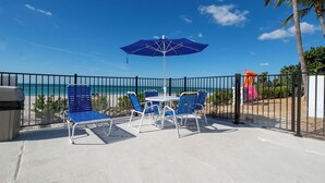 Un patio con sillas y mesa azules, una sombrilla azul y vista a la playa.