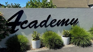 A sign with the word "Academy" in large letters, surrounded by potted plants and a clear sky. - Academy Motor Inn (Tauranga)