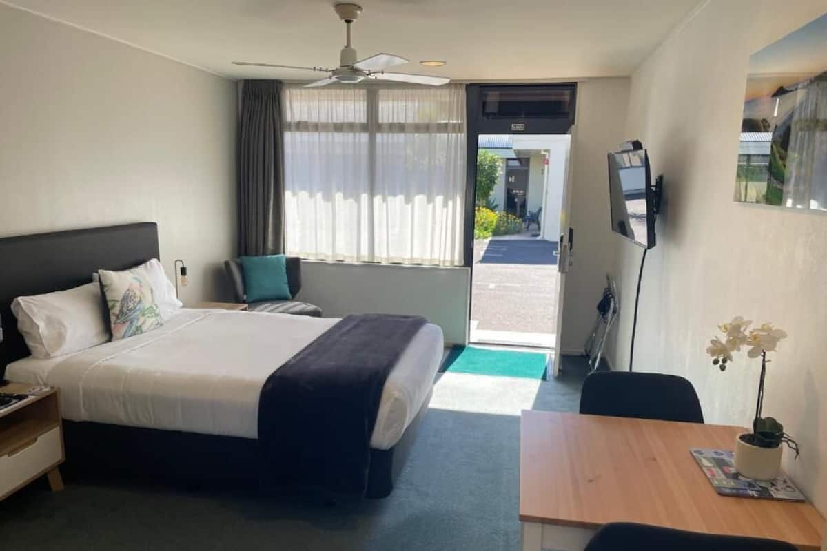 A hotel room with a bed, a desk, a chair, a TV, and a window with curtains.
