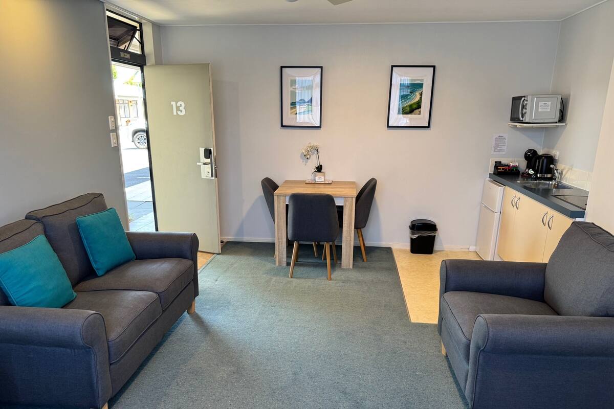 A compact living space with two sofas, a dining table, a small kitchen area, and a door marked with the number 13.