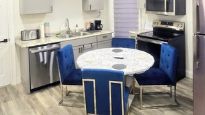 A compact kitchen with a round table, blue chairs, and modern appliances.