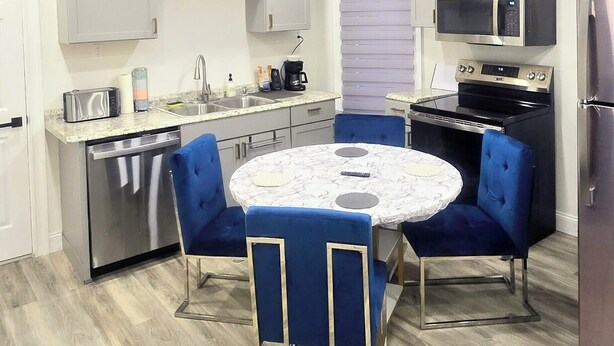 Una cocina compacta con una mesa redonda, sillas azules y electrodomésticos modernos.
