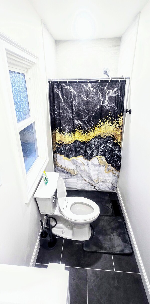 A small bathroom with a toilet, a shower curtain with a marble pattern, and a window with a blue pattern.