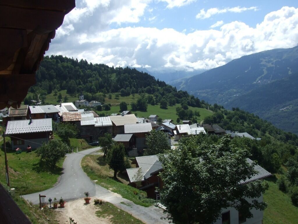 A village with houses and a winding road surrounded by green hills and mountains.