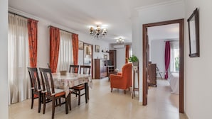 A dining area with a table, chairs, and a chandelier. There is a hallway leading to a bedroom.