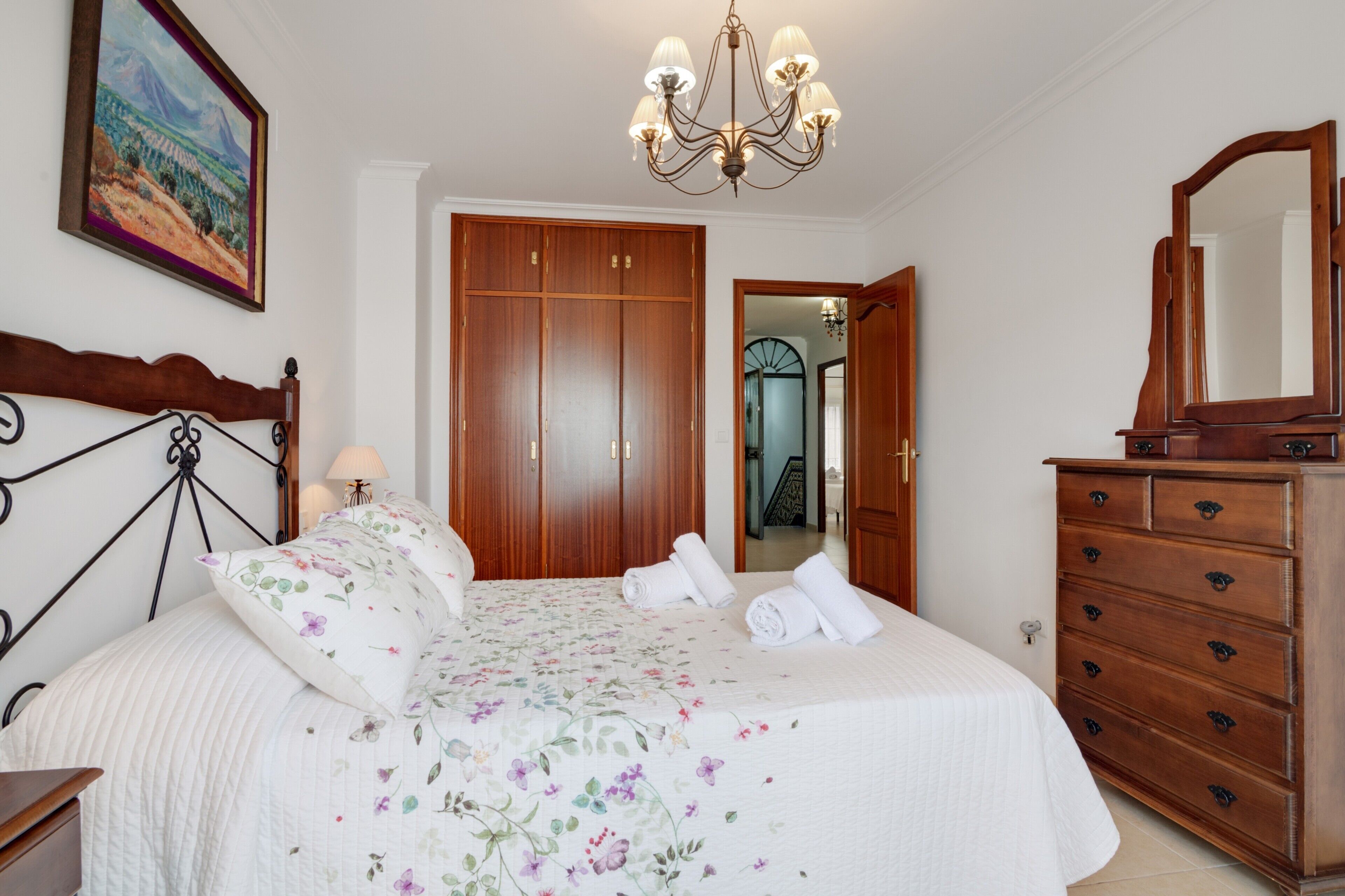A bedroom with a bed, wooden wardrobe, dresser, and a chandelier.