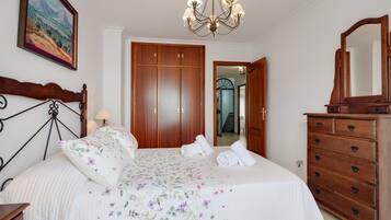 A bedroom with a bed, wooden wardrobe, dresser, and a chandelier.
