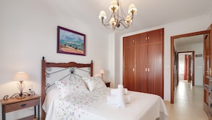 A bedroom with a wooden bed, a nightstand with a lamp, a painting on the wall, and a wooden wardrobe.