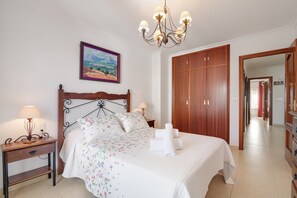 A bedroom with a wooden bed, a nightstand with a lamp, a painting on the wall, and a wooden wardrobe.
