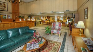 A spacious lobby with a green leather sofa, a wooden reception desk, and a chandelier. - Westgate Inn (Coudersport)