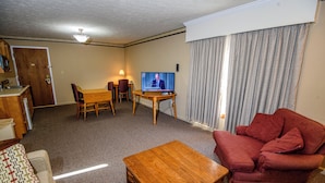 A living room with a wooden coffee table, a red sofa, a television on a stand, and a dining area with a table and chairs. - Westgate Inn (Coudersport)