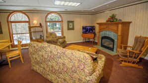 A living room with a floral sofa, wooden chairs, a fireplace, and a television. - Westgate Inn (Coudersport)