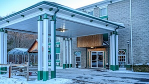 A building with a covered entrance, a wooden structure to the left, and a snow-covered ground. - Westgate Inn (Coudersport)