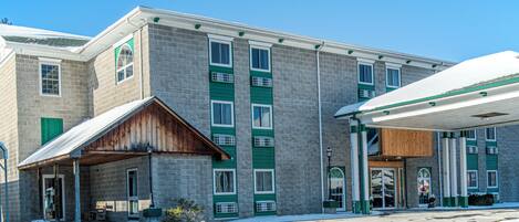 A two-story building with a stone facade, green window frames, and a covered entrance.