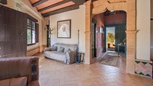 Un salón espacioso con un sofá estampado, una puerta de madera oscura y un suelo de baldosas.