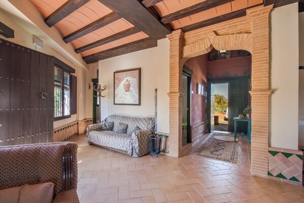 A spacious living area with a patterned sofa, a dark wooden door, and a tiled floor.