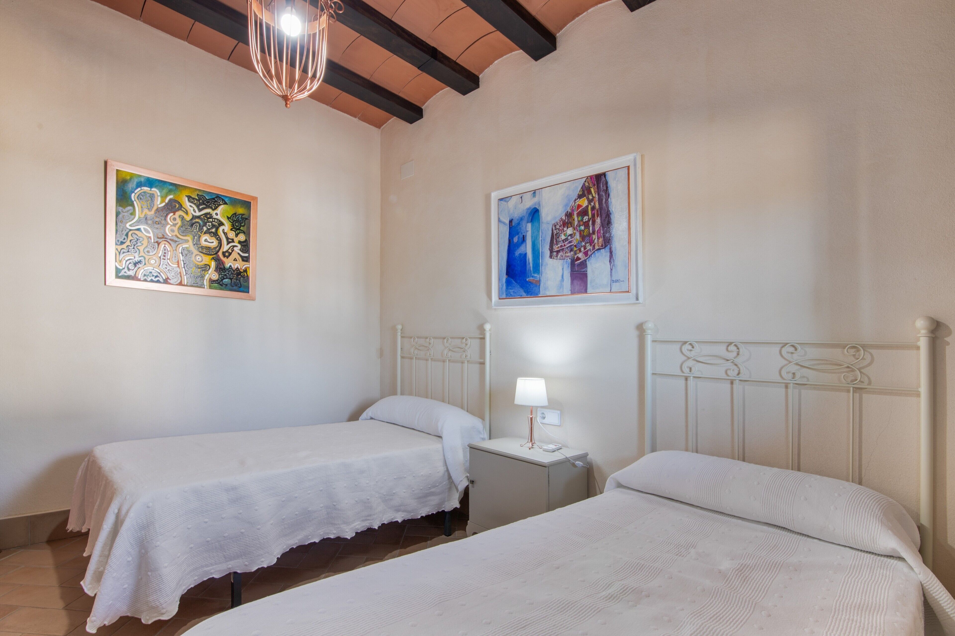 Un dormitorio con dos camas, una mesita de noche con lámpara y dos cuadros en la pared.