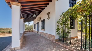 Un espacio al aire libre cubierto con suelo de ladrillo, paredes blancas y una pérgola con plantas trepadoras.
