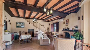 Amplia sala de estar con techo alto, vigas de madera, chimenea y una escalera que conduce a otro nivel.