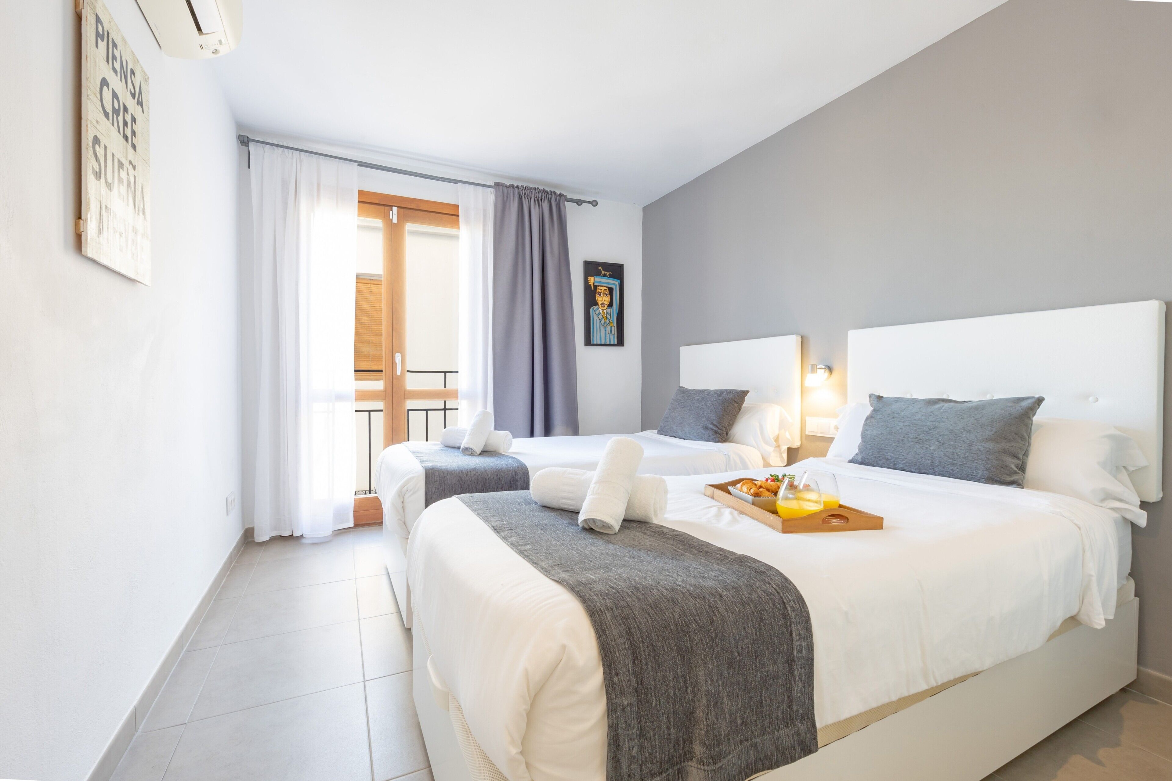 Een moderne hotelkamer met twee bedden, een ontbijtplateau en een schilderij aan de muur.