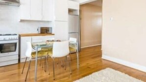A modern kitchen with white cabinets, a stainless steel range hood, and a dining area with a glass table and white chairs.