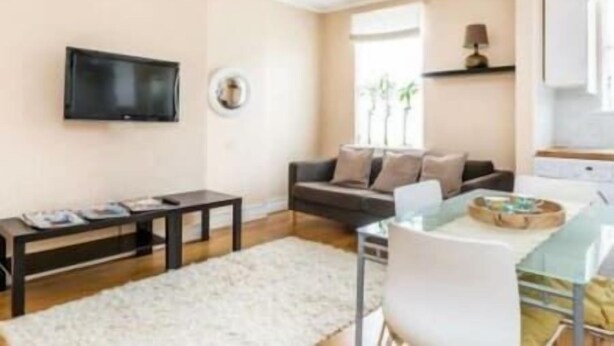 A modern living room with a flat-screen TV, a sofa, a coffee table, and a dining area with a glass top table.