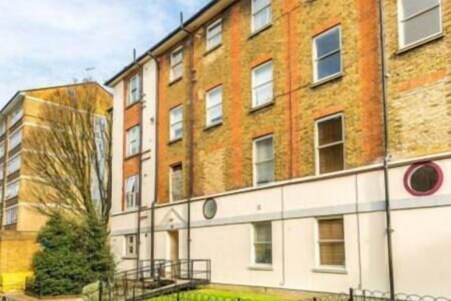 A multi-story residential building with a brick facade, multiple windows, and a small front garden.