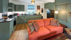 A modern kitchen with green cabinets, a central island, and a red sofa with patterned cushions. - Ddwylig Isaf Farmhouse - UK48624 (Rhyl and Prestatyn)
