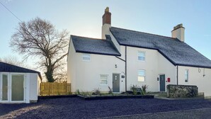 A two-story house with a dark tiled roof, a chimney, and a small front garden with plants and a wooden fence. - Ddwylig Isaf Farmhouse - UK48624 (Rhyl and Prestatyn)