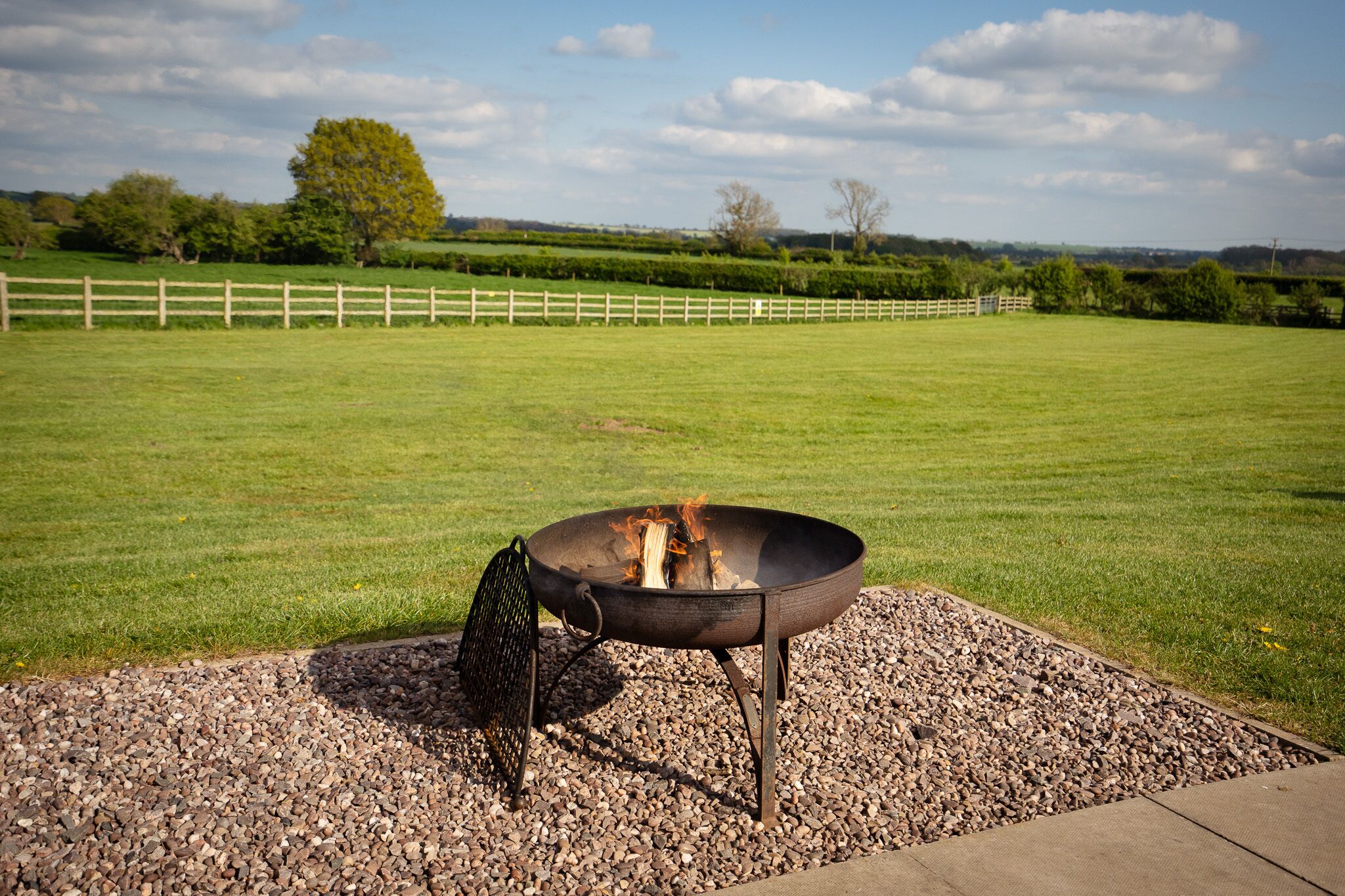 A fire pit with a metal chair in a grassy outdoor area with a wooden fence in the background.