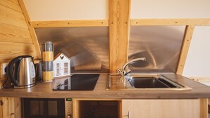 A compact kitchen with wooden cabinetry, a stainless steel sink, a kettle, and a small house-shaped container. - Rural Ensuite Wooden Cabin With Wood Fired Hot Tub (Tamworth)