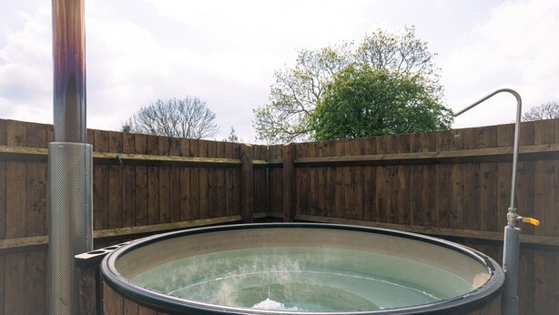 A hot tub with a wooden surround and a metal structure on one side. - Rural Ensuite Wooden Cabin With Wood Fired Hot Tub (Tamworth)