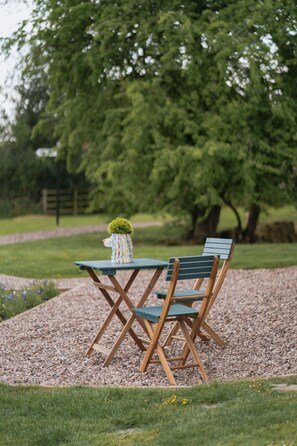 A wooden table and chair set on a gravel path with a small potted plant.
