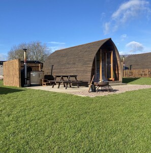 Un bâtiment rustique en bois, doté d’un toit en pente, d’une grande porte ouverte et d’un foyer au premier plan.
