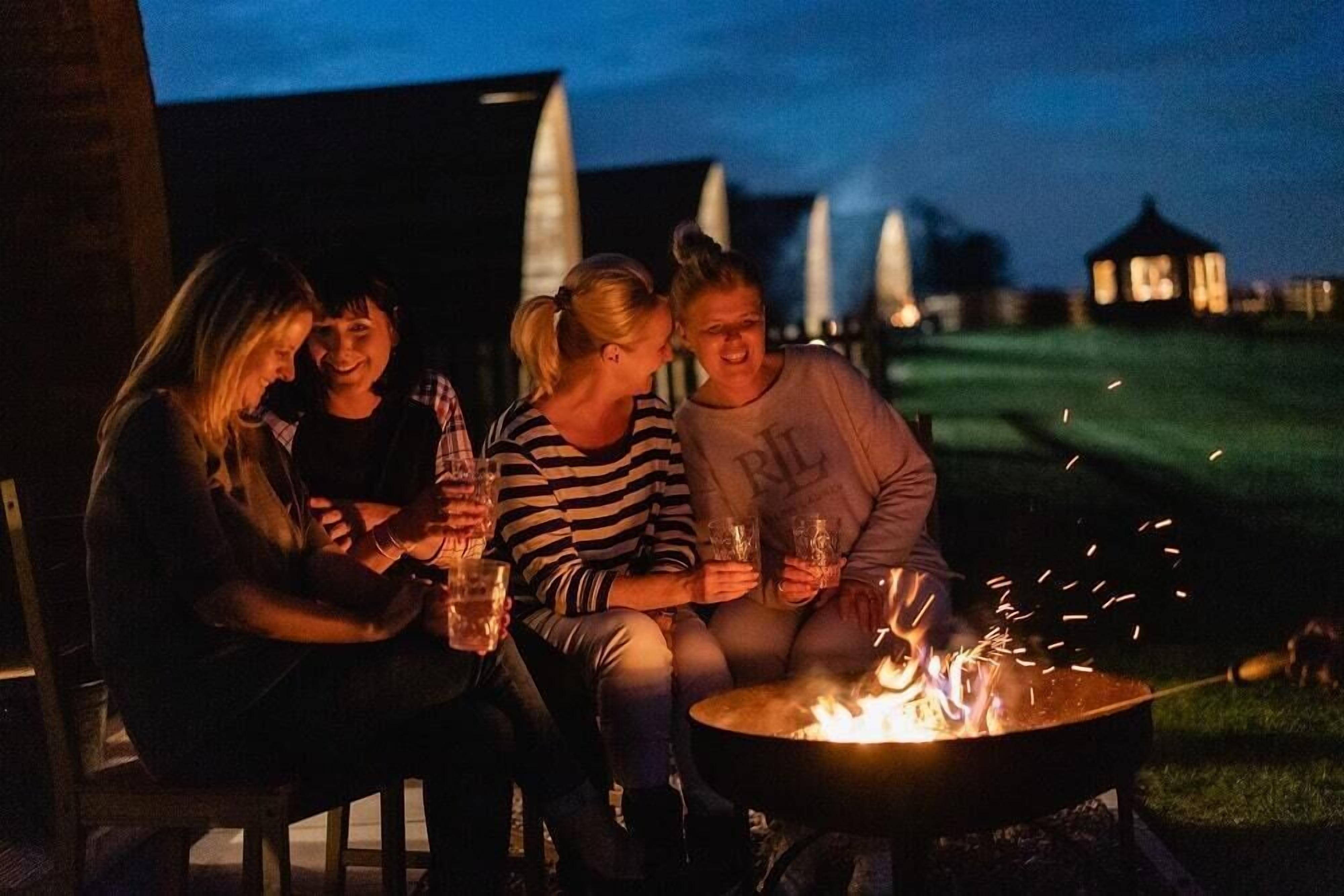 Vier Personen sitzen nachts an einem Lagerfeuer.