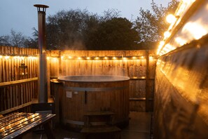 A wooden hot tub with a metal frame, surrounded by a wooden fence and string lights. - Ensuite Wooden Cabin in Rural Staffordshire (Tamworth)