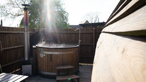 A hot tub with a wooden exterior, a metal heater, and a small step for access. - Ensuite Wooden Cabin in Rural Staffordshire (Tamworth)