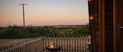 Eine Terrasse mit Feuerstelle, einem Holzzaun und Blick auf die Landschaft.