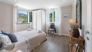 A bedroom with a bed, a chair, a wooden side table, and a large mirror. - Terraced House 'Due Ulivi' with Private Terrace, Garden, and Wi-Fi (Lavagna)